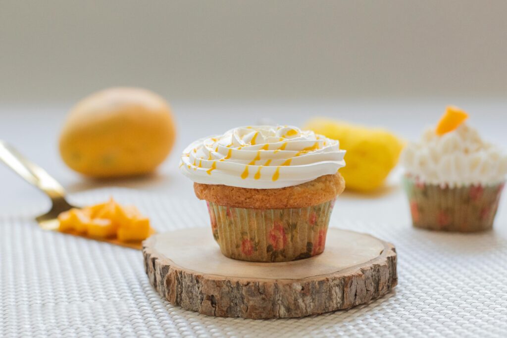 Close-up of a mango cupcake with cream frosting, surrounded by fresh mango pieces.